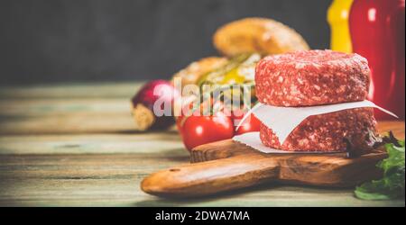 Hausgemachte Hamburger. Rohes Rindfleisch Frikadellen und Ciabatta Brot mit anderen Zutaten für die Hamburger auf Holz- Hintergrund Stockfoto