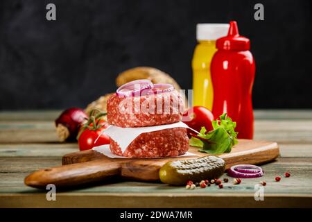 Hausgemachte Hamburger. Rohes Rindfleisch Frikadellen und Ciabatta Brot mit anderen Zutaten für die Hamburger auf Holz- Hintergrund Stockfoto