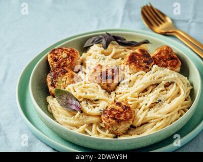 Zucchini Parmesan Fleischbällchen mit Pasta Carbonara in grüner Platte über blauer Leinentischdecke. Nahaufnahme von cremiger Carbonara mit Fleischbällchen. Stockfoto