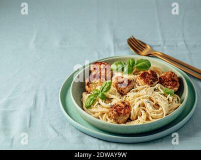 Zucchini Parmesan Fleischbällchen mit Pasta Carbonara in grüner Platte über blauer Leinentischdecke. Nahaufnahme von cremigem Carbonara mit Kopierraum Stockfoto