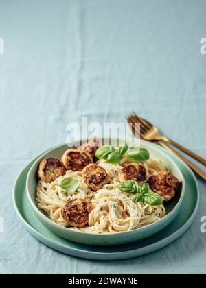 Zucchini Parmesan Fleischbällchen mit Pasta Carbonara in grüner Platte über blauer Leinentischdecke. Cremige Carbonara mit Copy Space Top. Vertikal Stockfoto