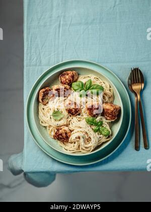 Zucchini Parmesan Fleischbällchen mit Pasta Carbonara in grüner Platte über blauer Leinentischdecke auf der Tischplatte. Cremige Carbonara mit Copy Space Top. Vert Stockfoto