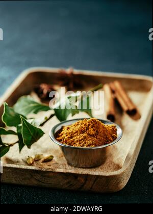 Indische oder pakistanische Masala Pulver und Gewürze auf Holztablett. Kleine Metallschüssel mit trockenem Curry Garam Masala Mix Gewürzmischung, grünes Lorbeerblatt, Zimt Stockfoto