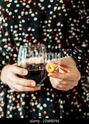 Unkenntlich Frau im festlichen Kleid hält Weinglas Becher und tarallini. Traditionelle italienische Snack Taralli oder Tarallini mit Rotwein in weiblichen h Stockfoto