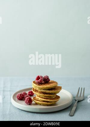 Glutenfreie Zucchini-Pfannkuchen mit Maismehl. Stapel von gesunden Zucchini Pfannkuchen auf Teller über Tischplatte mit blauer Leinentischdecke. Minimalistisches Bild Stockfoto