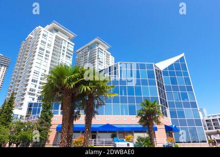 Gebäude mit Glasfassade und Appartementgebäude mit Palmen vor blauem Himmel. Stockfoto