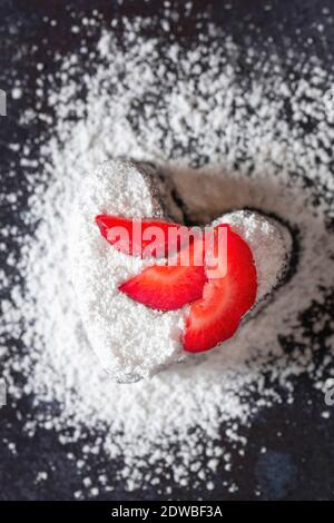 Herzförmige Brownie mit Puderzucker bestäubt und mit Erdbeerscheiben verziert. Stockfoto