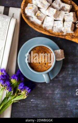 Türkischer Kaffee, serviert in einer grauen Kaffeetasse und begleitet von türkischen Köstlichkeiten, wilden Blumen und Zeitung auf dunklem Hintergrund. Stockfoto