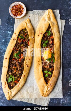 Türkische Pide gefüllt mit Rindfleisch und ein Ei auf einem Stück Backpapier auf einem dunklen Hintergrund fotografiert. Stockfoto