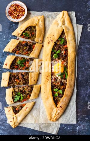 Türkische Pide gefüllt mit Rindfleisch und ein Ei auf einem Stück Backpapier auf einem dunklen Hintergrund fotografiert. Stockfoto