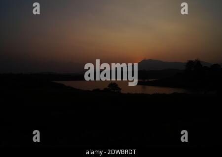 Sonnenuntergang im dunklen Hintergrund hinter dem Hügel in karapuzha Damm, Wayanad, Kerala, Indien. Es ist einer der größten Erdstaumauer in Kerala. Stockfoto