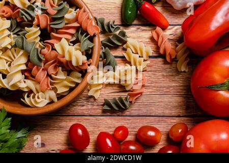 Terracotta-Schüssel mit dreifarbigen Fusilli-Nudeln und Kirsche und runde Tomaten, Chili, Knoblauch und Petersilie. Konzept der Lebensmittelrohstoffe. Gehackter Winkel Stockfoto