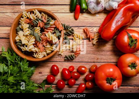 Terracotta-Schüssel mit dreifarbigen Fusilli-Nudeln und Kirsche und runde Tomaten, Chili, Knoblauch und Petersilie. Konzept der Lebensmittelrohstoffe. Gehackter Winkel Stockfoto