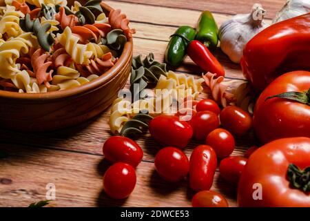 Terracotta-Schüssel mit tricolor Fusilli Pasta und Kirsche und runde Tomaten, Chilischoten, Knoblauch und Petersilie. Konzept der Lebensmittelrohstoffe. 45 Grad Winkel Stockfoto