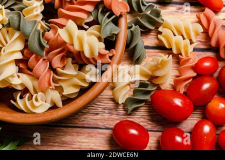 Terracotta-Schüssel mit dreifarbigen Fusilli-Nudeln und Kirsche und runde Tomaten, Chili, Knoblauch und Petersilie. Konzept der Lebensmittelrohstoffe. Gehackter Winkel Stockfoto