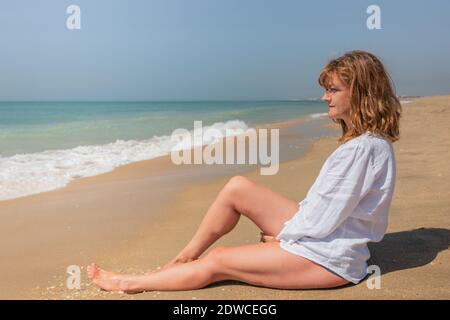 Frau, die am Strand sitzt und den Horizont betrachtet Stockfoto