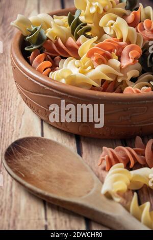 Schüssel mit dreifarbigen italienischen Fusilli Pasta auf einem Holzbrett mit einigen gefallenen Nudeln. Stockfoto