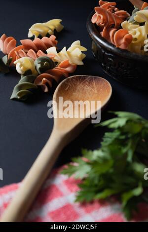 Ebano Schüssel mit tricolor Fusilli Nudeln und Kirsche und runde Tomaten, Chili, Knoblauch und Petersilie. Konzept der Lebensmittelrohstoffe. 45 Grad Winkel. Stockfoto