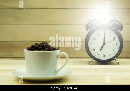 Uhr zeigt sieben Uhr morgens an. Uhr und Kaffeesorten als Hintergrund. Das Konzept des Aufwachens oder Aufwachens von einem Wecker Stockfoto