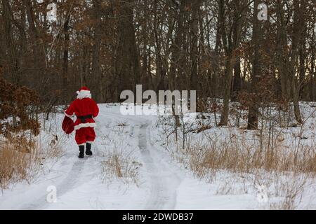 Weihnachtsmann beim Spaziergang durch den Winterwald mit Weihnachtsgeschenken In einer roten großen Tasche Stockfoto