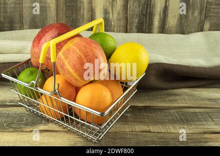 Frische und gesunde Früchte in einem Korb auf einem Hintergrund von Holzlatten mit Platz für Text. Mandarinen und Orangen, Grapefruit und Limette, Apfel und avoca Stockfoto