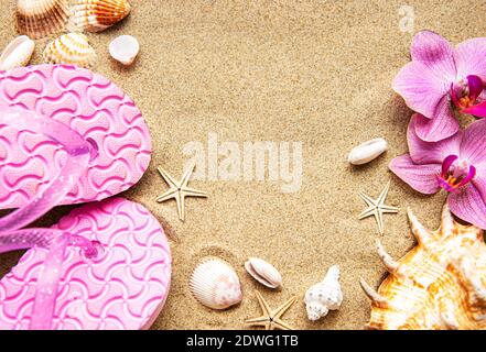 Flip Flops im Sand mit Seesternen und Orchideenblumen. Konzept „Sommerzeit am Strand“. Sommerstrand. Stockfoto