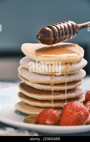 Heiße Pfannkuchen mit Honig auf einem Teller. Leckeres Gericht zum Frühstück. Honig fließt von einem Holzstock auf eine Schüssel. Hausgemachtes Essen Stockfoto