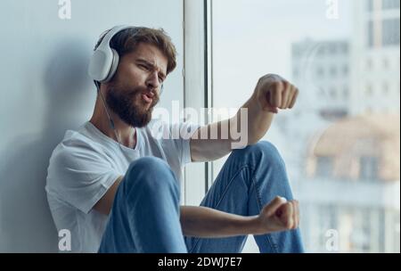 Ein Mann mit Kopfhörern sitzt auf der Fensterbank und hört zu Zur Musik Imitation Fahren eines Autos Lenkrad Studio Stockfoto