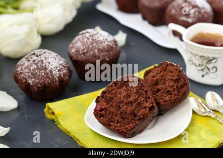 Schokoladen-Muffins mit Kirsche, bedeckt mit Puderzucker auf dunklem Hintergrund Stockfoto