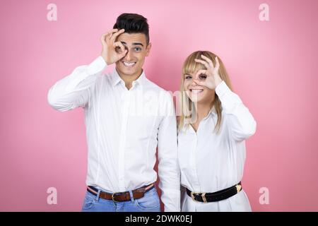 Junges Paar von Freundin und Freund über isoliert rosa Hintergrund tun ok Geste schockiert mit lächelndem Gesicht, Auge durch die Finger schauen Stockfoto