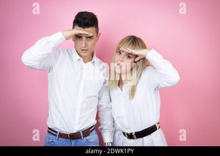 Junges Paar von Freundin und Freund über isoliert rosa Hintergrund sehr glücklich und lächelnd suchen weit weg mit Hand über Kopf. Suchkonzept. Stockfoto