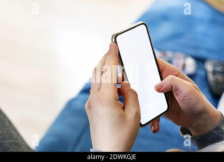 Kaukasische Frau Hände halten ein Smartphone in einem modernen Wohnzimmer. Weißer Bildschirm für den Kopierbereich. Mustervorlage. Wireless-Technologie und tragbare Geräte Stockfoto
