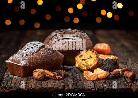 Drei Weihnachtsbrot, Stollen, mit Mandarine, auf einem Holztisch mit Struktur, vor dem Hintergrund von verschwommenen Lichtern in Bokeh. Zu Weihnachten. Stockfoto