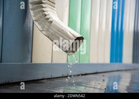 Regenwasser fließt über einen Abfluss vom Dach des Gebäudes. Entfernung von Regenwasser. Downpipe Weiß Stockfoto