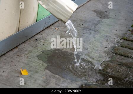 Regenwasser fließt über einen Abfluss vom Dach des Gebäudes. Entfernung von Regenwasser. Downpipe Weiß Stockfoto