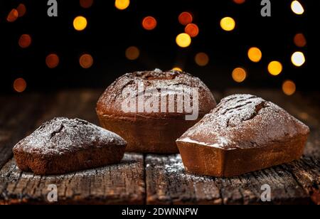 Drei Weihnachtsbrot, Stollen, auf einem Holztisch mit Struktur, vor dem Hintergrund von verschwommenen Lichtern in Bokeh. Stockfoto