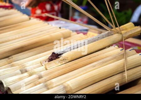 Street Food Markt in Asien. Ein Mann verkauft Reis in Bambusstielen. Stockfoto