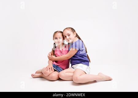 Fun Mädchen, Schwestern sitzen auf dem Boden auf den Knien und Umarmung auf weißem Hintergrund Stockfoto