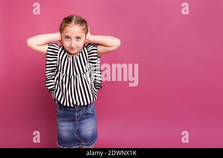 Kleines Mädchen bedeckt ihre Ohren mit Händen auf einem rosa Hintergrund. Stockfoto