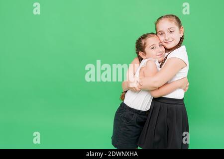 Zwei kleine Schwestern in Schuluniform umarmen sich gegenseitig, Spaß auf grünem Hintergrund Stockfoto