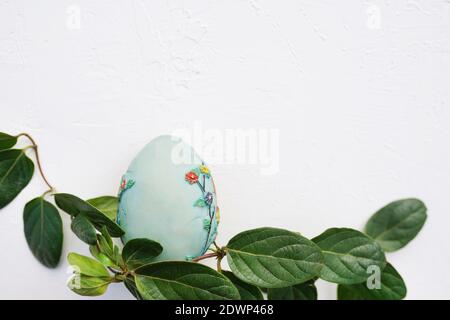 Frohe Ostern. blaues Osterei mit grünen Blättern auf weißem Texturhintergrund. Keine Verschwendung, kein Kopierplatz Stockfoto
