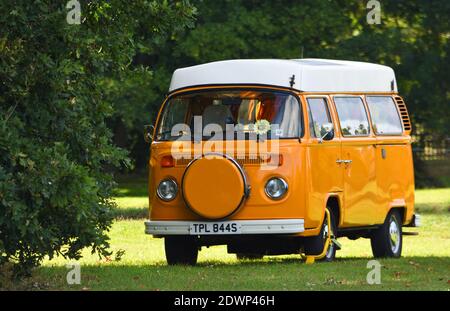 Classic Orange VW Camper Van auf Dorfgrün geparkt. Stockfoto