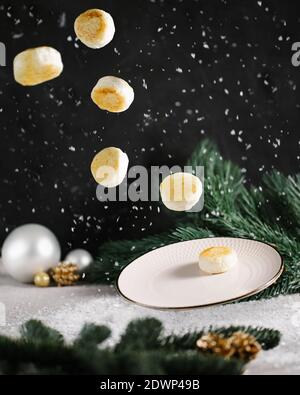 Levitation mit einem fliegenden Hüttenkäse Pfannkuchen Winter eingerichtet Weihnachtsstimmung auf dem schwarzen Hintergrund mit grünen Kiefernabies Verzweigungen Stockfoto