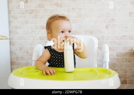 Liebenswert Baby Mädchen trinkt Milch aus Flasche sitzt in der Stuhl Stockfoto