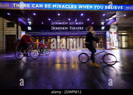 London, Großbritannien. - 21. Dezember 2020: Eine Familie radelt am verlassenen Eingang des Dominion Theaters an der Tottenham Court Road vorbei, der wegen Einschränkungen durch Coronaviren nur wenige Tage vor Weihnachten geschlossen ist. Stockfoto