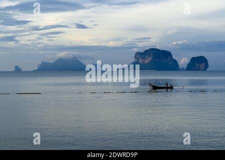 Ein Mann in seinem Fischerboot, der von seinem morgendlichen Fisch zurückkommt, durin einem wunderschönen Morgenlicht am Pranang Cave Beach, Railay, Krabi, Thailand Stockfoto