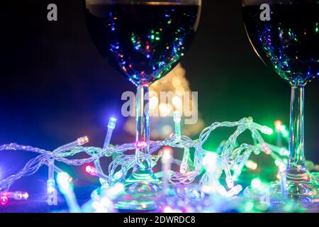 Zwei Gläser auf dem Hintergrund eines leuchtenden Weihnachtsbaums und eine bunte Girlande auf einem dunklen Nachtshintergrund. Neujahrsfeier... Stockfoto