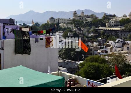 Morgen Blick auf die Dachterrasse von Udaipur City Palace und Pichola See. Bergkette und blauer Himmel auf dem Hintergrund. Orange leuchtend winkende Flagge. Rajasthan Stockfoto