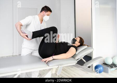 Physiotherapeut mit Schutzmaske, die eine Massage für einen Patienten gibt. Wiedereröffnung mit physiotherapeutischen Sicherheitsmaßnahmen bei der Pandemie Covid-19. Osteopathie, therapeutische Chiromassage. Hochwertige Fotos Stockfoto