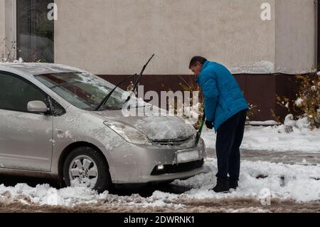 Krasnodar, Russland - Dezember 21 2020: Mann in blauer Jacke, der ein schneebedecktes Auto nach Schneesturm putzt Stockfoto